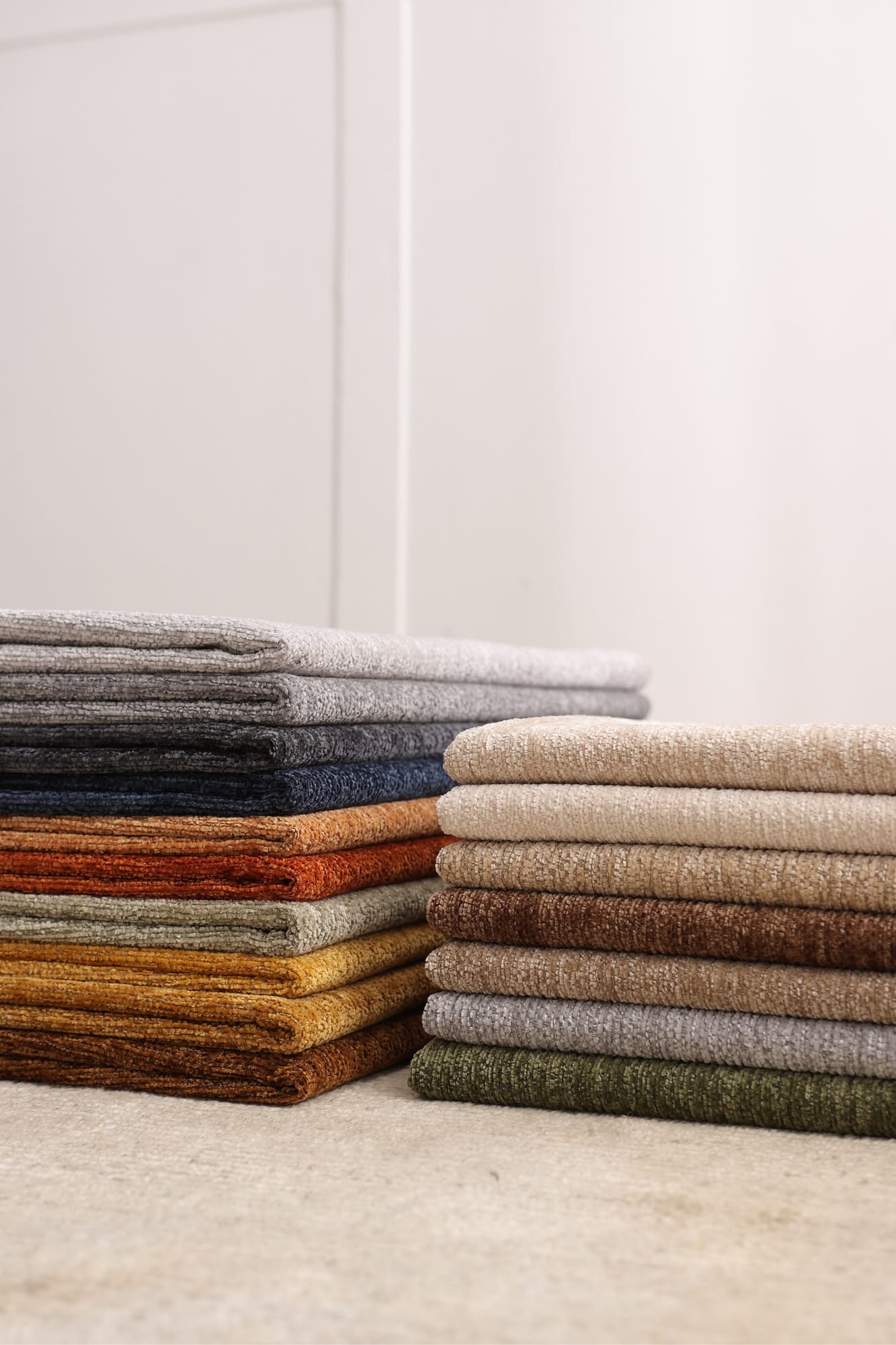 Two stacks of folded woven fabrics in warm neutrals, rust and green