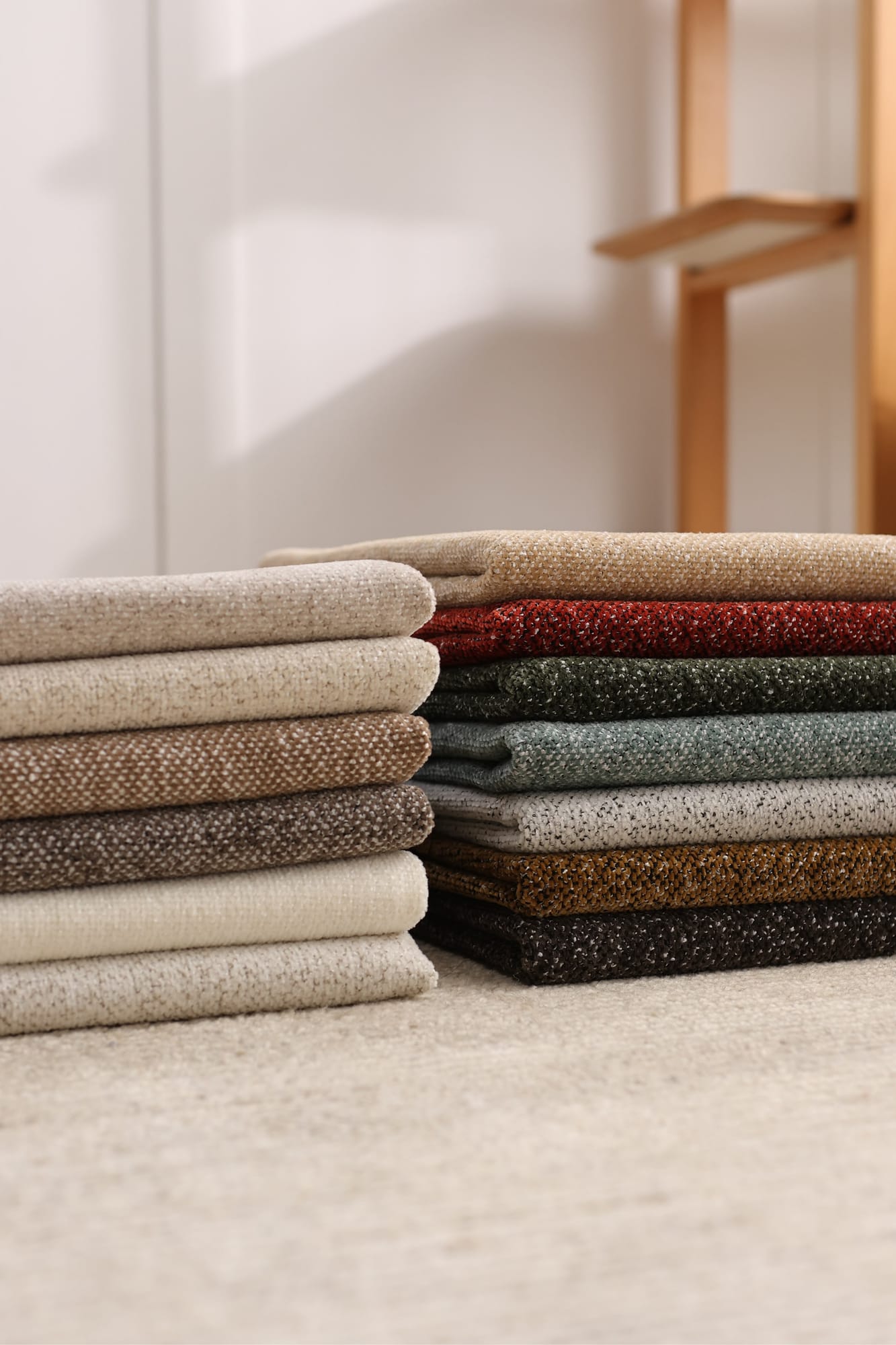 Folded stacks of woven upholstery fabric in neutral and earthy colourways by a bright window